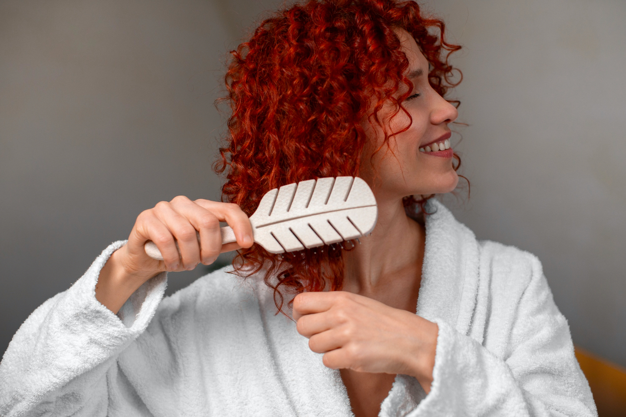 Mujer en albornoz se cepilla el pelo / FREEPIK