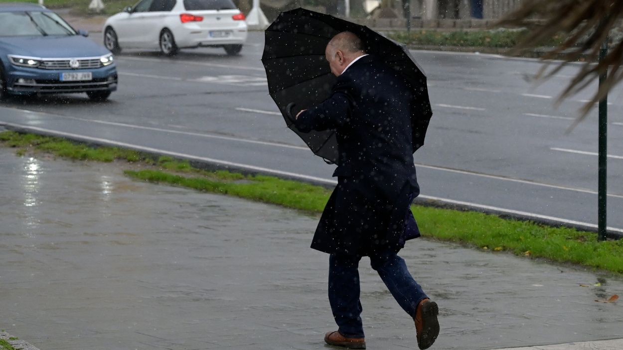 Un hombre con paraguas trata de refugiarse del viento y de la lluvia. EP.