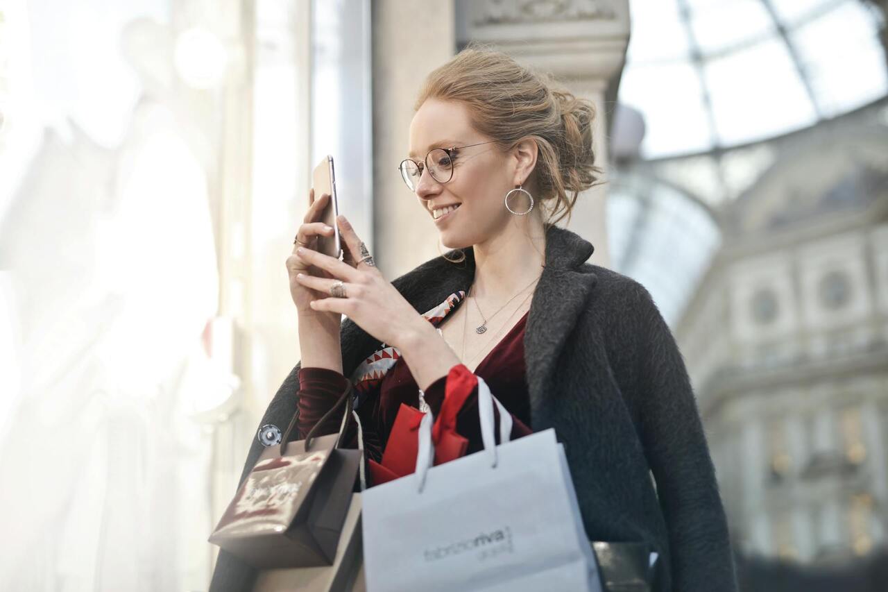Compradora con bolsas consulta su móvil / PEXELS