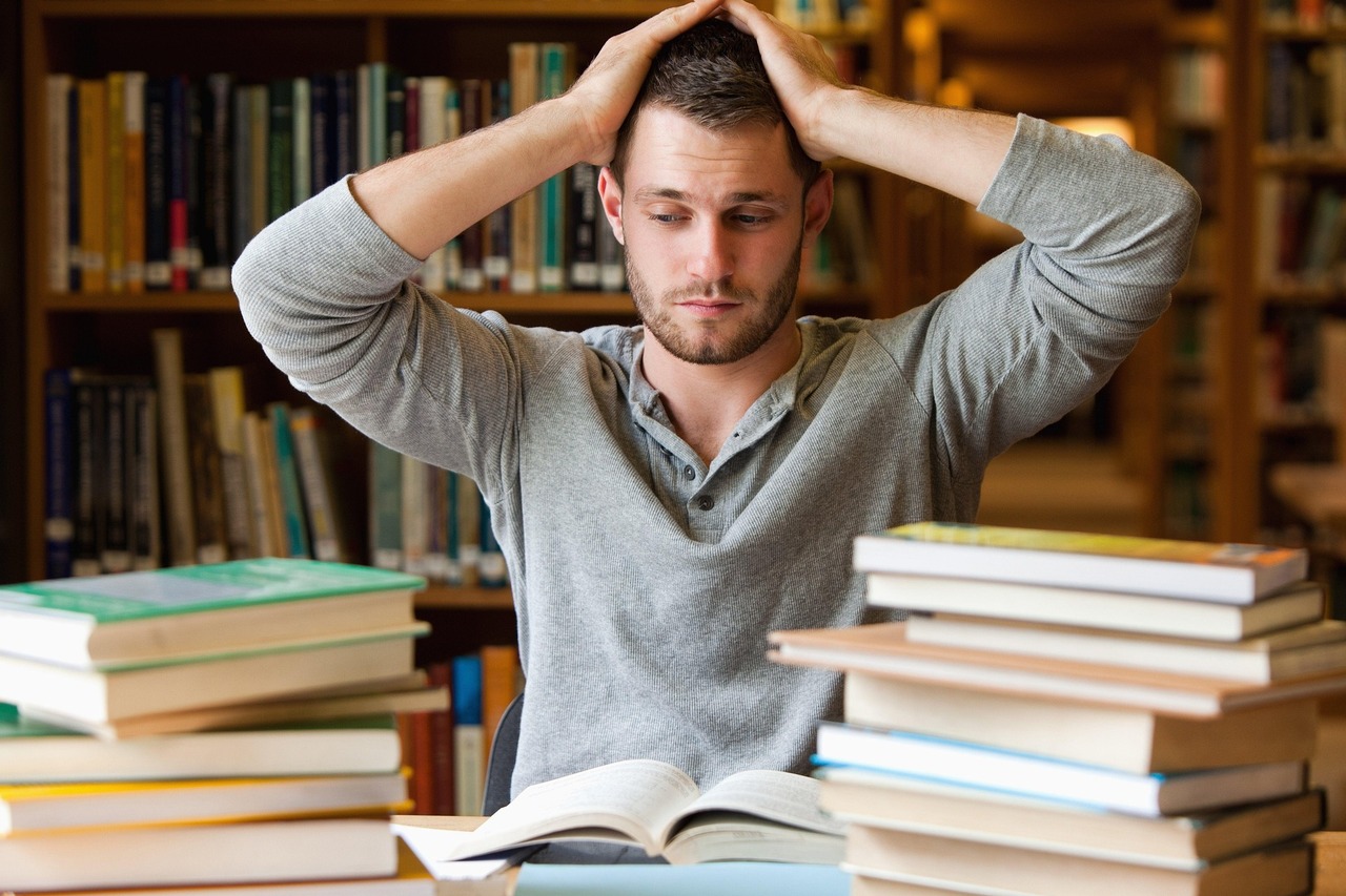 Estudiante rodeado de libros se lleva las manos a la cabeza / PIXABAY