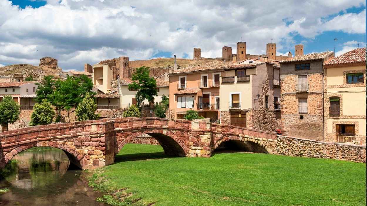 El puente románico sobre el río Gallo, con la silueta del castillo al fondo y el conjunto urbano a sus pies.