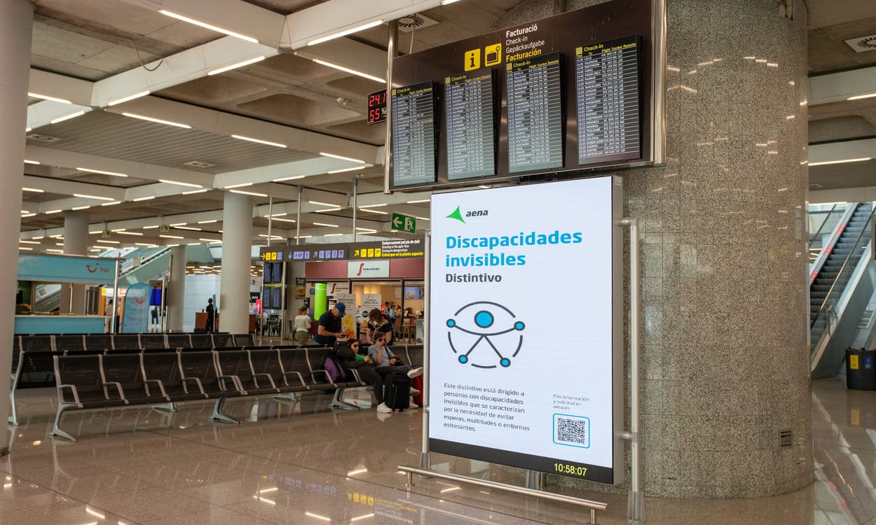 Panel informativo sobre el distintivo para discapacidades invisibles en el Aeropuerto de Palma de Mallorca, una iniciativa que permite al personal identificar y ofrecer apoyo a quienes puedan necesitarlo durante su tránsito. Aena