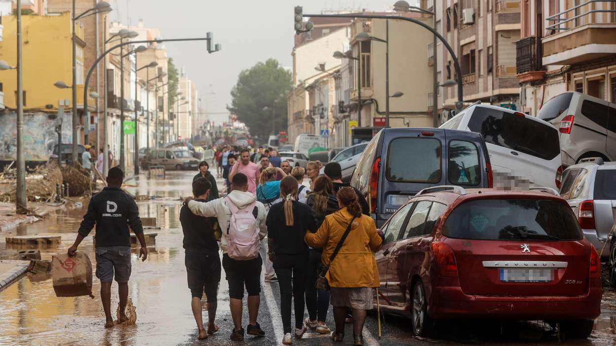 Varias personas junto a coches destrozados tras el paso de la DANA por el barrio de La Torre de Valencia