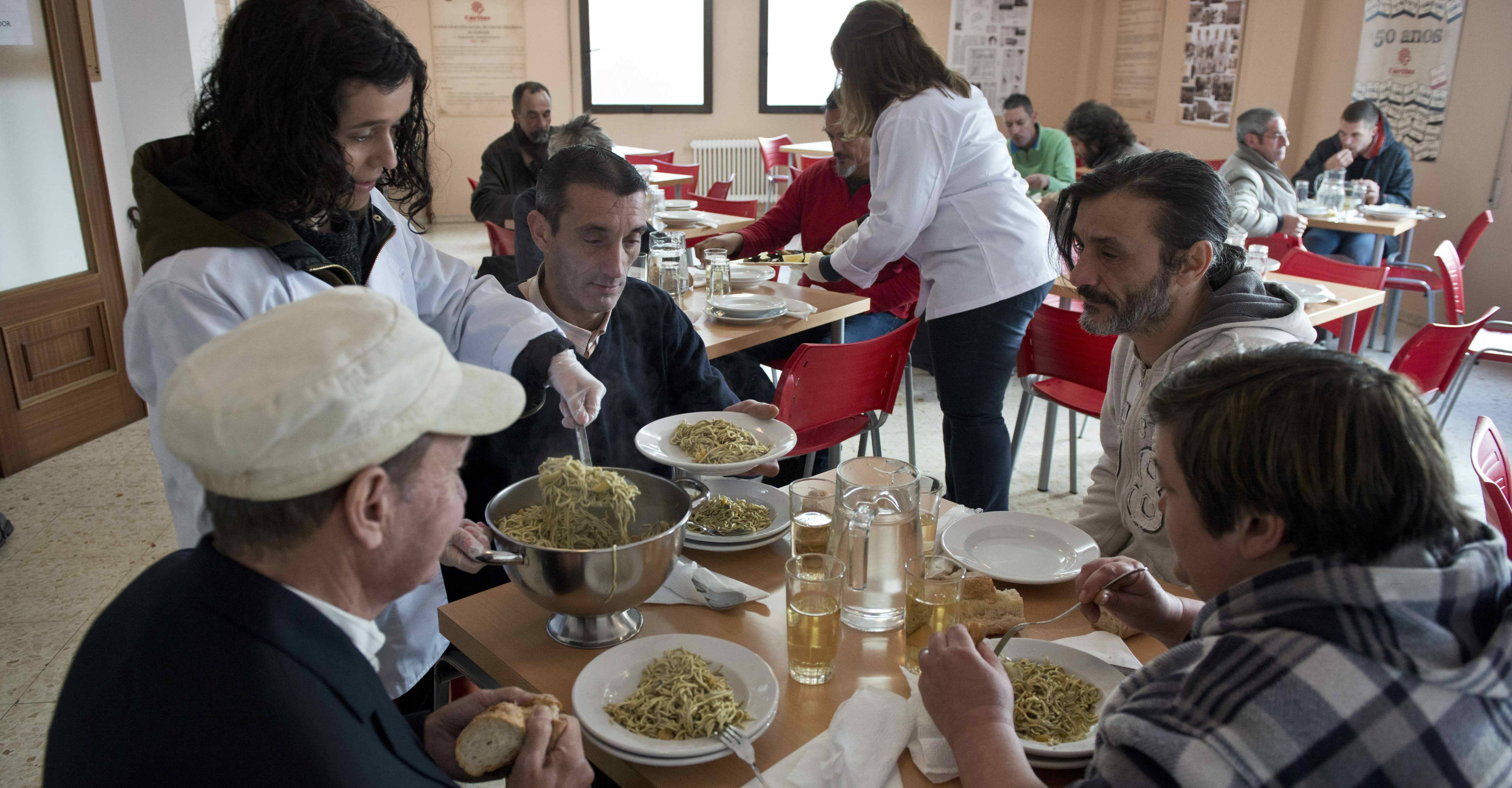 Una voluntaria sirve comida a un grupo de personas sin recursos en el comedor social de Cáritas situado en el antiguo convento de las Siervas de María, en Ourense. 