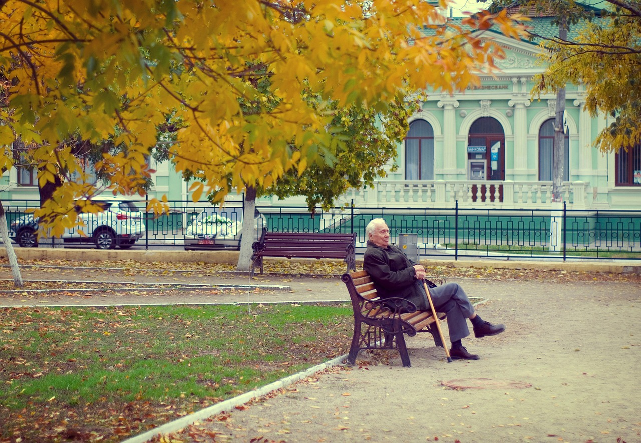 Un señor mayor sentando en un banco del parque