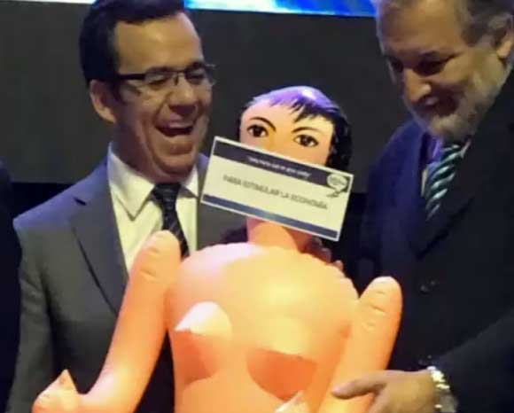 Captura del momento en que el ministro de Economía de Chile recibe el regalo de una muñeca hinchable