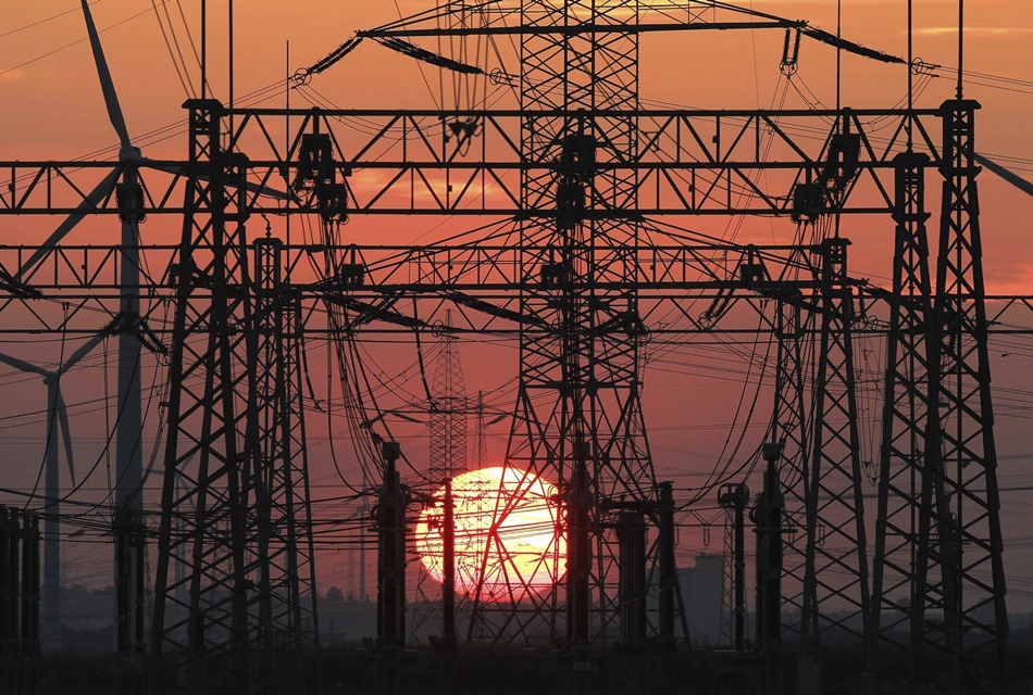 En la imagen, una puesta de sol junto al tendido eléctrico y unos molinos de viento. 