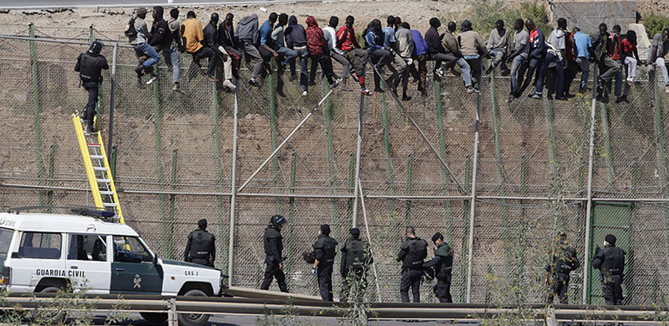 Un grupo de inmigrantes en las vallas observados por guardias civiles. 