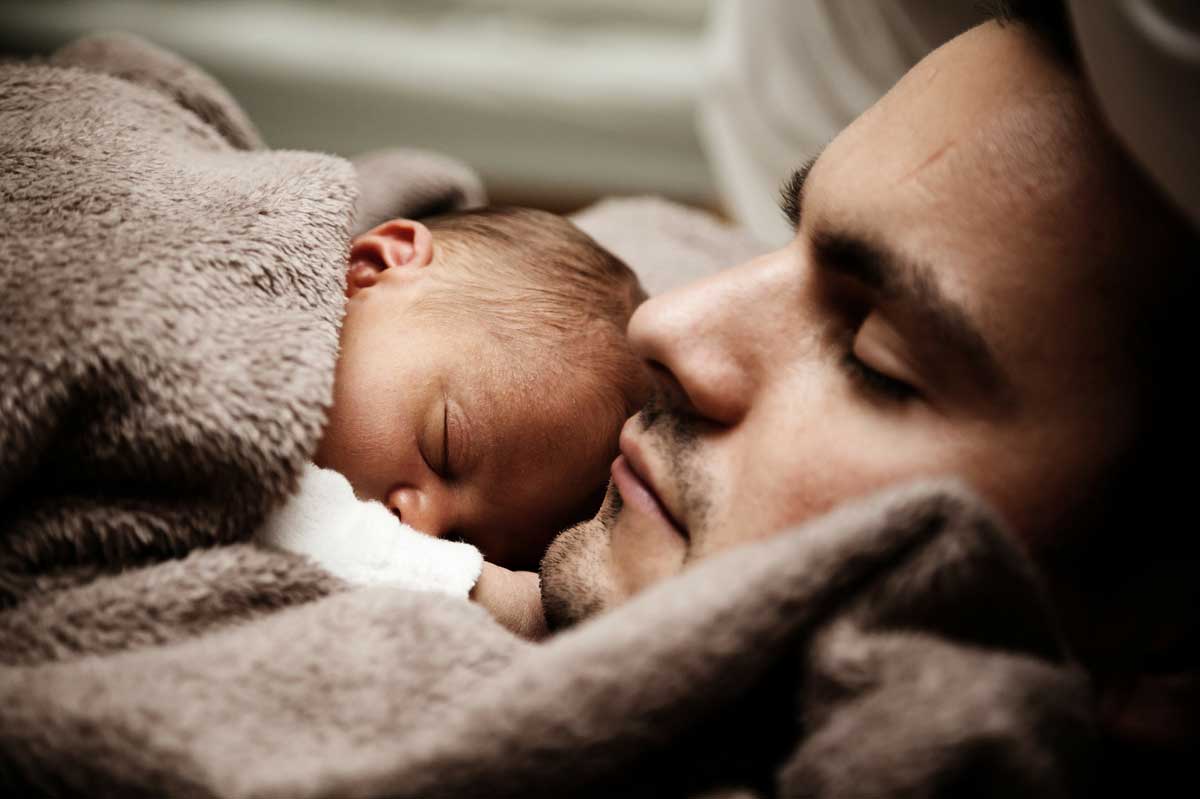 Imagen de un padre durmiendo con su hijo recien nacido. 
