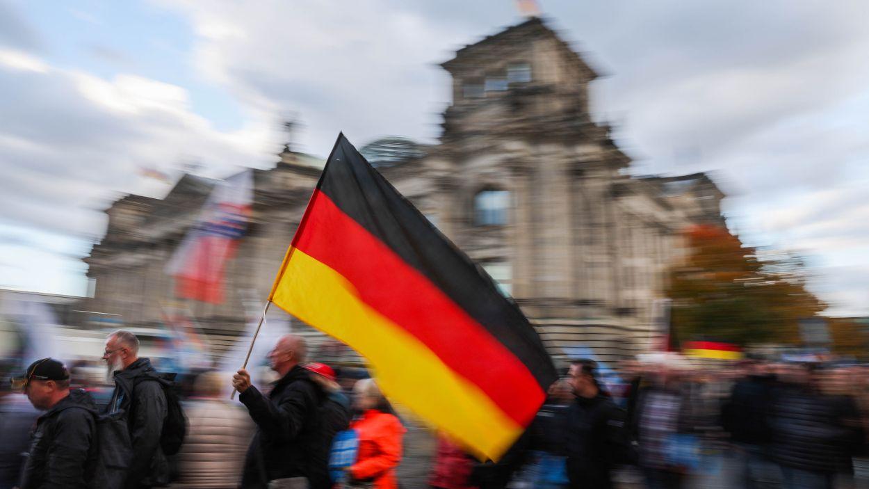 Un hombre con una bandera alemana pasa frente al edificio del Reichstag durante una protesta del partido AfD bajo el lema "Seguridad energética y protección contra la inflación: nuestro país primero". Foto: Christoph Soeder/dpa.