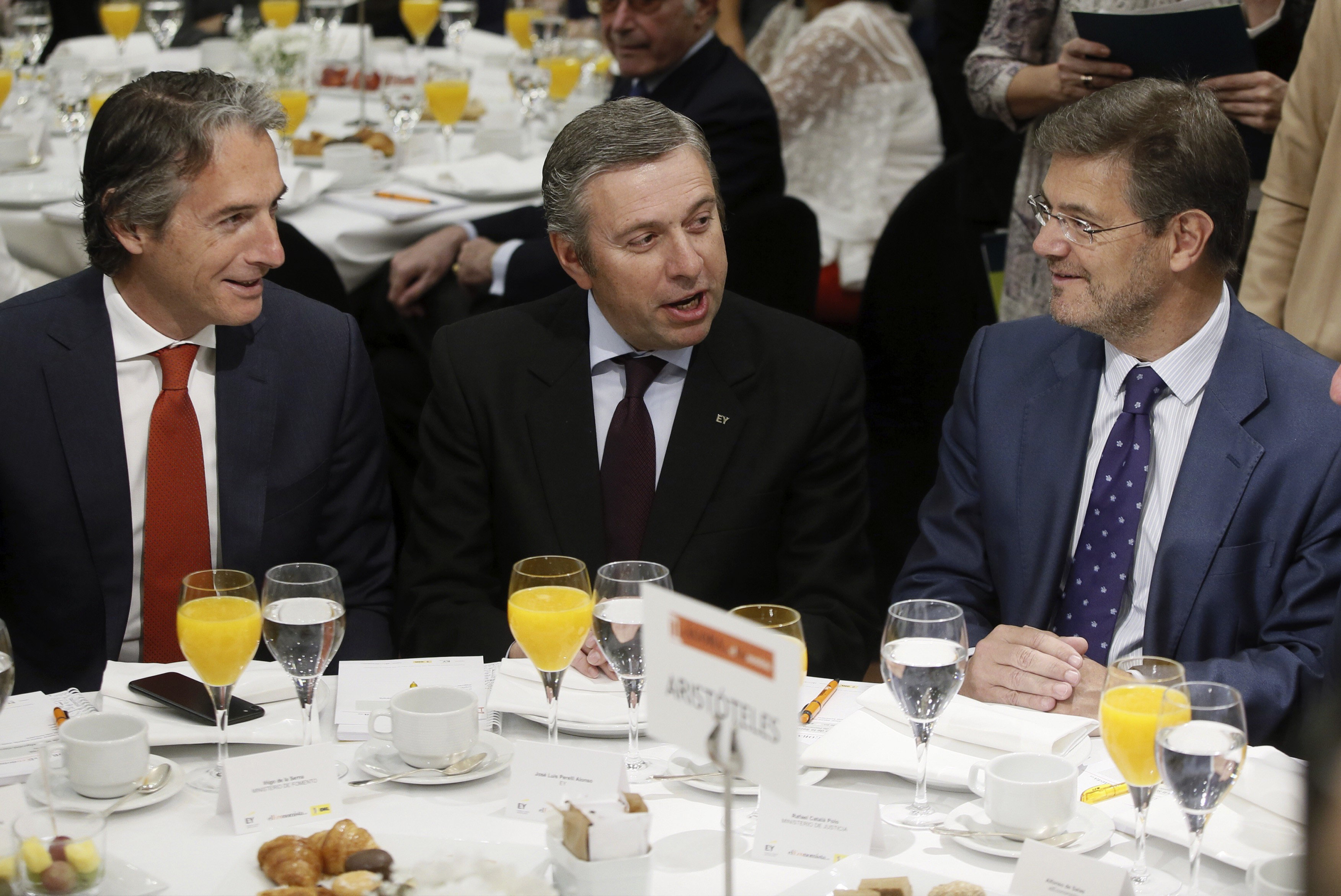 El ministro de Fomento, Íñigo de la Serna (i), conversa con el ministro de Justicia, Rafael Catalá (d), en presencia del presidente de EY España, José Luis Perelli, poco antes de su intervención hoy en un desayuno-coloquio en "El Ágora de El Economista