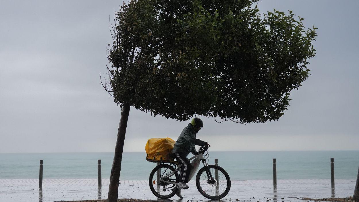Un hombre en bicicleta bajo la lluvia en la playa de la Barceloneta. EP.