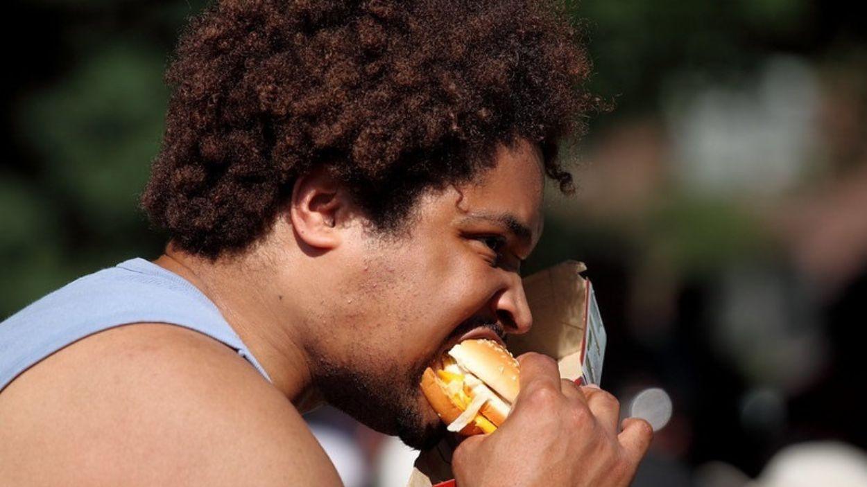 Hombre comiendo una hamburguesa en la calle. EP