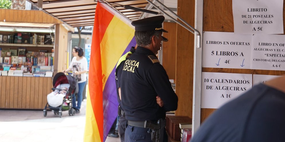 Dos policías locales ordenando al foro de la Memoria retirar la bandera republicana de su caseta en la Feria del Libro.