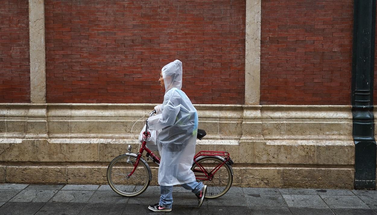 Una persona bajo la lluvia con bicicleta y chubasquero en Málaga. EP