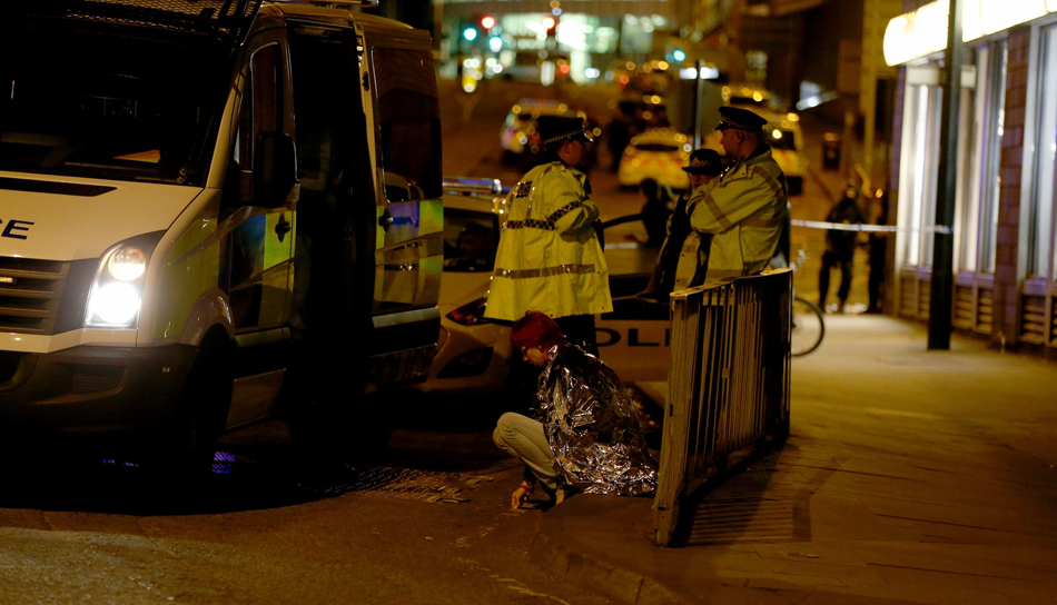 Una mujer sentada en una calle cerca al Manchester Arena, junto a un grupo de policías, después de las explosiones.