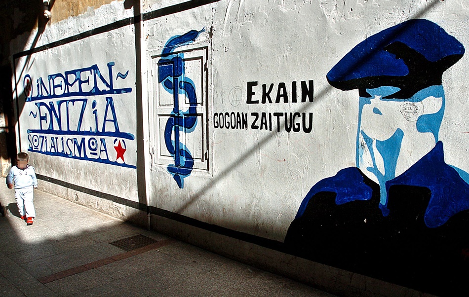  Un niño pasa junto a un mural que representa a un encapuchado junto al anagrama de ETA