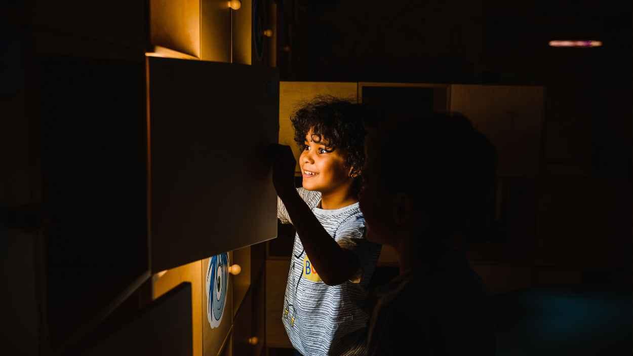 Un niño interactúa con una exhibición educativa brillante, destacando la curiosidad y el aprendizaje. Pexels.