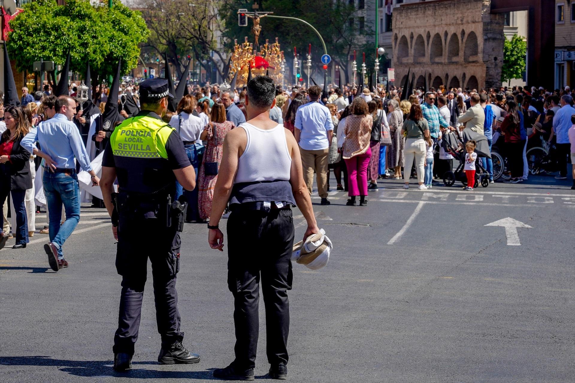 Un policía municipal y un costalero viendo el cortejo de la Hermandad de la Sed por a Av Luis Montoto. Imagen archivo / EP