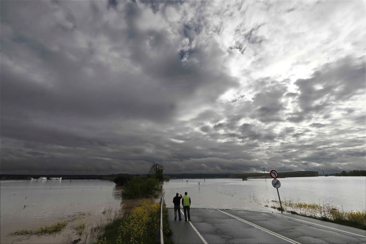 Dos personas toman imagenes de la carretera N-113 que permanece cortada hacia Castejón tras el desbordamiento del Rio Ebro