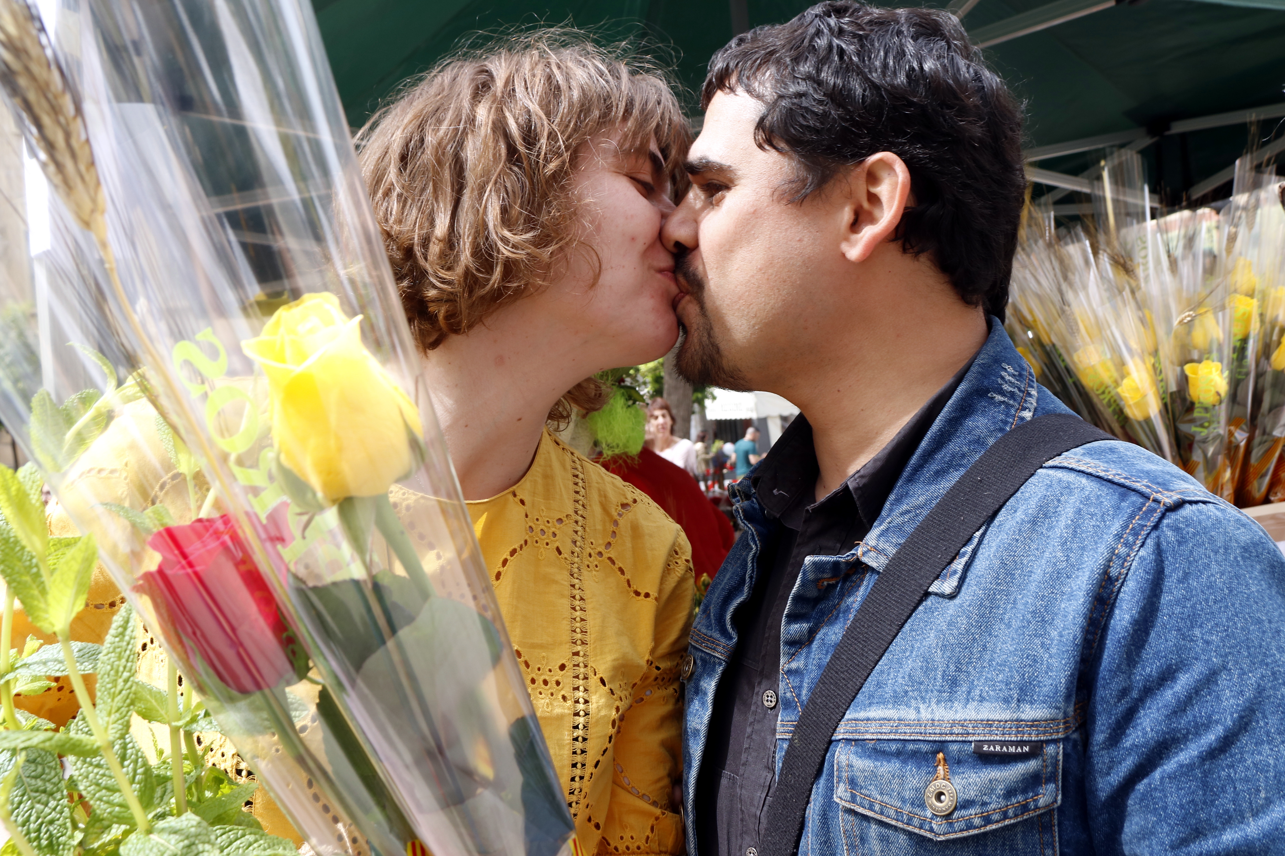 Una pareja de Tarragona dándose un beso en una parada de rosas durante la diada de Sant Jordi en la Rambla Nova, y ella lleva una rosa amarilla en las manos