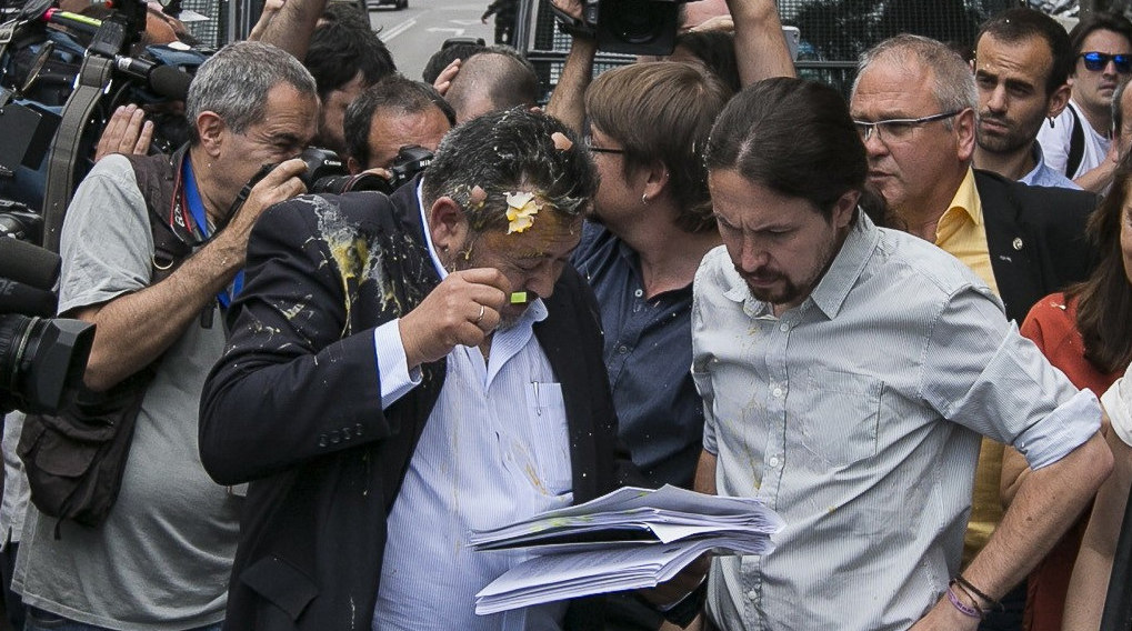 Julio Sanz, presidente de la Federación Profesional del Taxi, recibe el impactoi de un huevo en la cabeza mientras conversa con el líder de Podemos, Pablo Iglesias. 