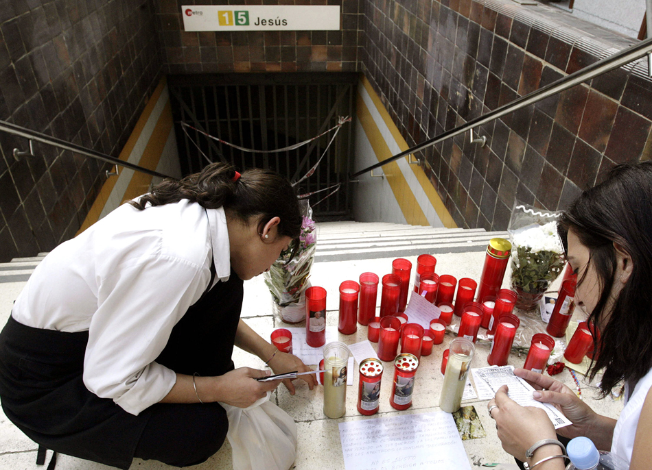 Dos jóvenes contemplan el altar de velas y mensajes de condolencia instalado en la entrada de la estación de metro. 