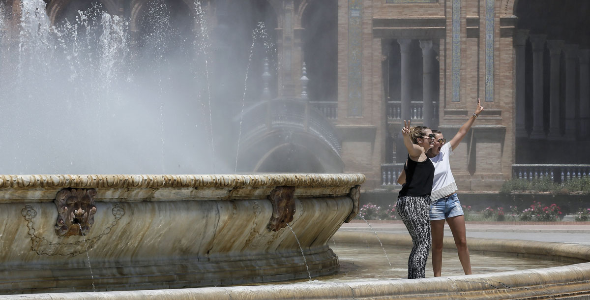 Jóvenes turistas franceses se refrescan del calor en una fuente de la Plaza de España de Sevilla