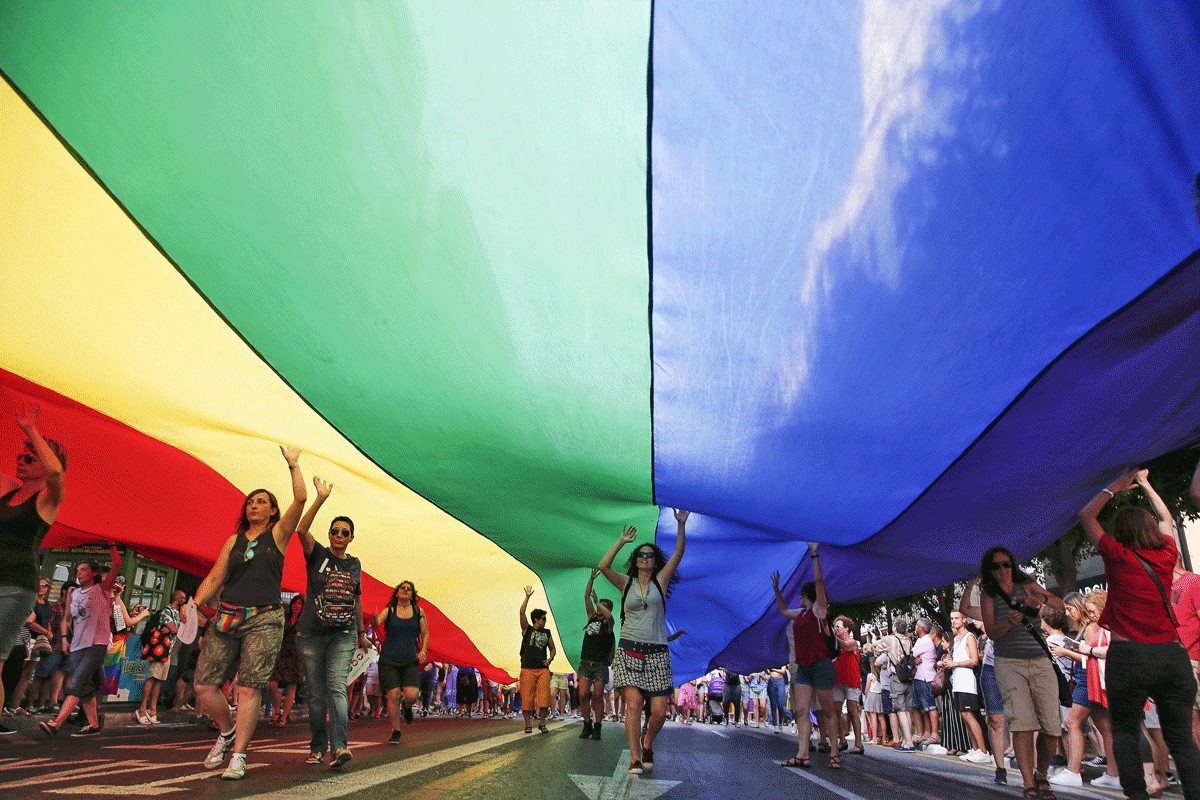 Varias personas portan una bandera arcoríris gigante.