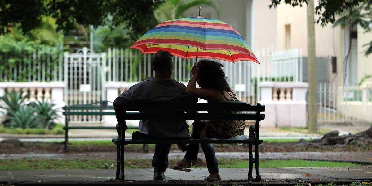 Una pareja conversa bajo la lluvia en un banco. 