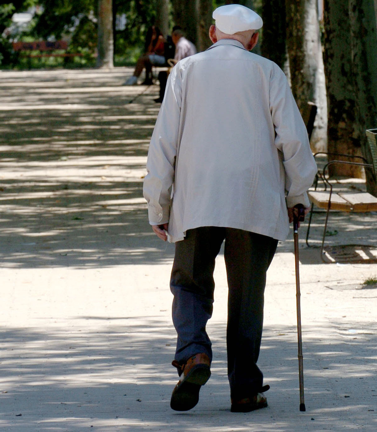 Un anciano caminando ayudado con un bastón.