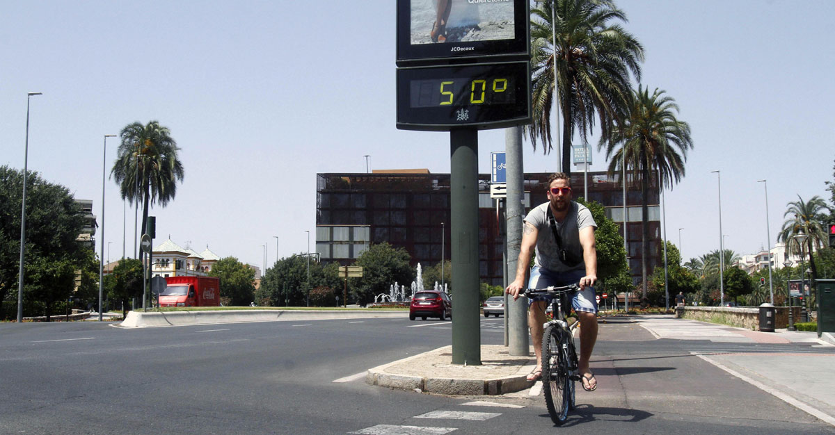 Un joven pasa con su bicicleta junto a un termómetro que marca 50 grados hoy en una calle de Córdoba. 