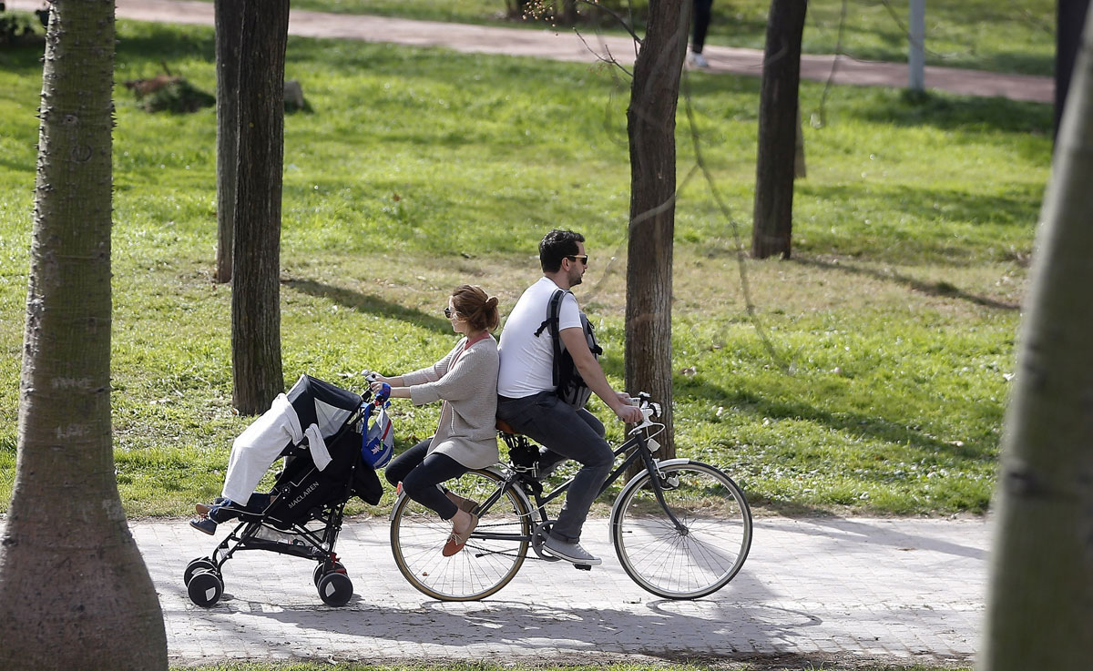 Una pareja pasea en bici con el carrito de bebe.