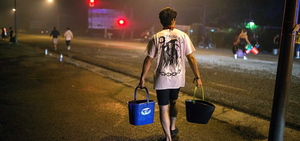 En la imagen, un hombre porta dos cubos de agua para ayudar a sofocar uno de los focos declarados en el centro de la ciudad de Vigo. 