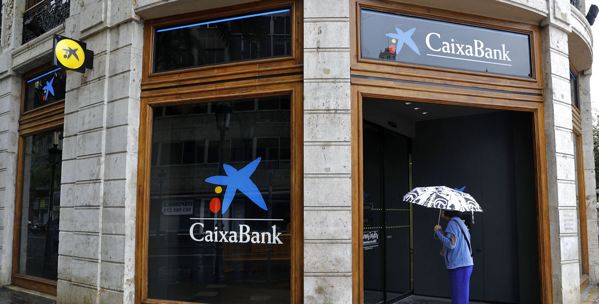 Una mujer observa el interior de la sede de Caixabank en la plaza del Ayuntamiento de Valencia. 