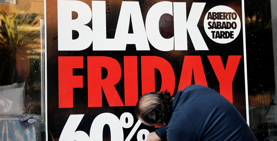 Un operario coloca un cartel en el escaparate de una tienda en la que anuncia grandes rebajas en el "Black Friday" o Viernes Negro