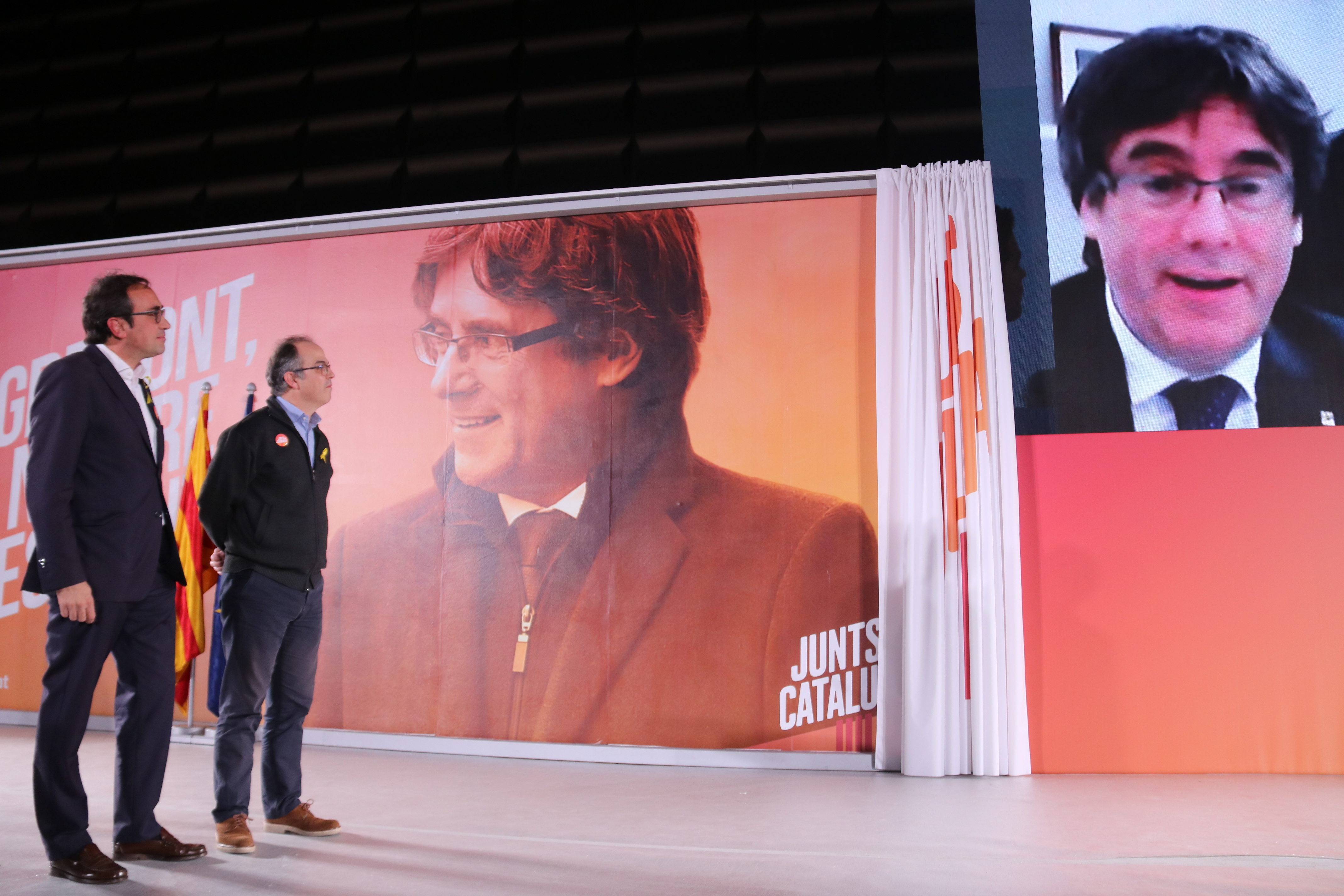 Los exconsellers Josep Rull y Jordi Turull atienden a una vídeo llamada de Puigdemont desde Bélgica durante un acto
