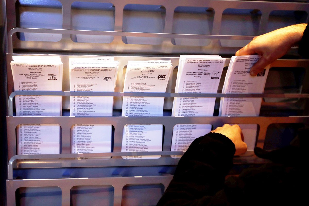 Un operario coloca papeletas electorales en una cabina en el Ayuntamiento de Barcelona.