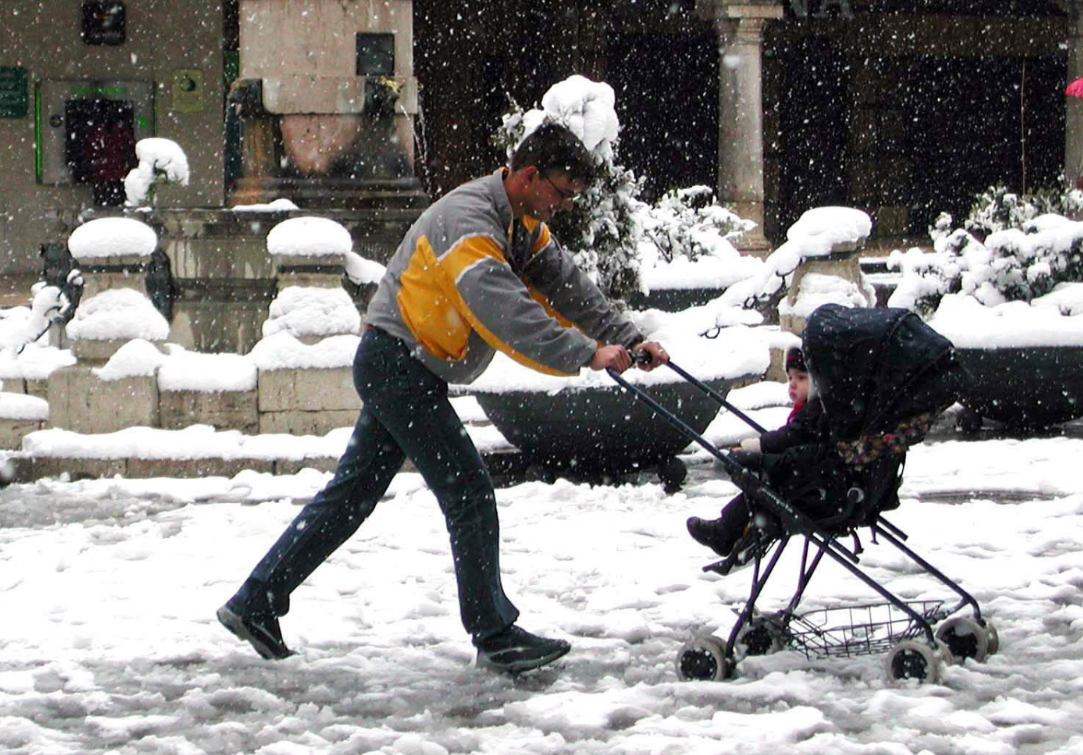 Un padre empuja el carrito de su bebé bajo la nieve. 
