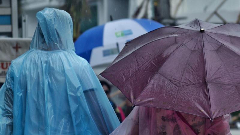 Dos personas con paraguas y chubasqueros pasen por la calle en un día de lluvias y tormentas. EP.