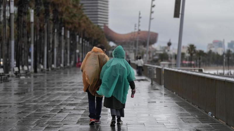 Vecinos de Barcelona pasean bajo la lluvia en la playa de la Barceloneta durante el temporal. EP.