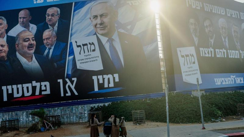 Transeúntes con cochecitos de bebé caminan por la acera bajo enormes vallas publicitarias de la campaña electoral que muestran al primer ministro Benjamin Netanyahu y figuras de la oposición en Tel Aviv. EP.