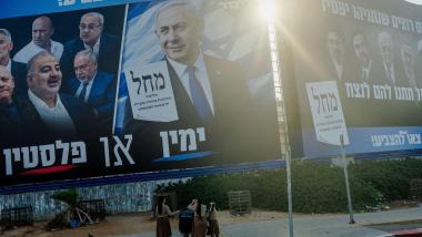 Transeúntes con cochecitos de bebé caminan por la acera bajo enormes vallas publicitarias de la campaña electoral que muestran al primer ministro Benjamin Netanyahu y figuras de la oposición en Tel Aviv. EP.