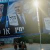 Transeúntes con cochecitos de bebé caminan por la acera bajo enormes vallas publicitarias de la campaña electoral que muestran al primer ministro Benjamin Netanyahu y figuras de la oposición en Tel Aviv. EP.