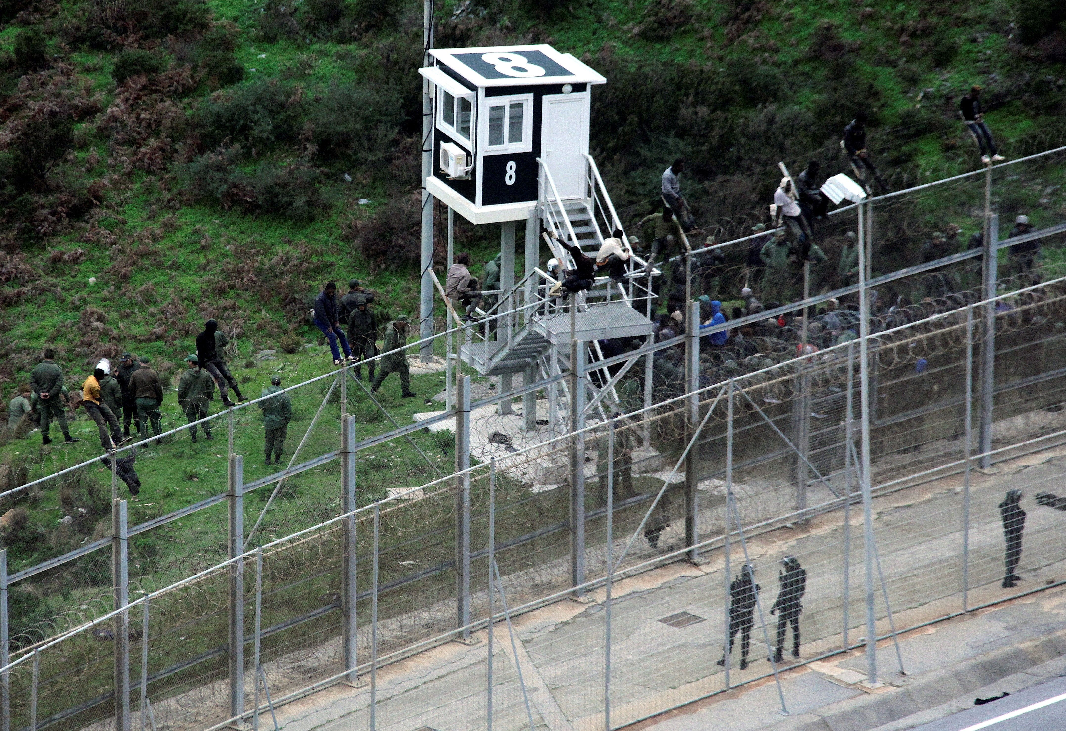 Inmigrantes custodiados por la policía marroquí, junto a la valla del perímetro fronterizo de Ceuta, en una imagen de archivo. EFE/Archivo