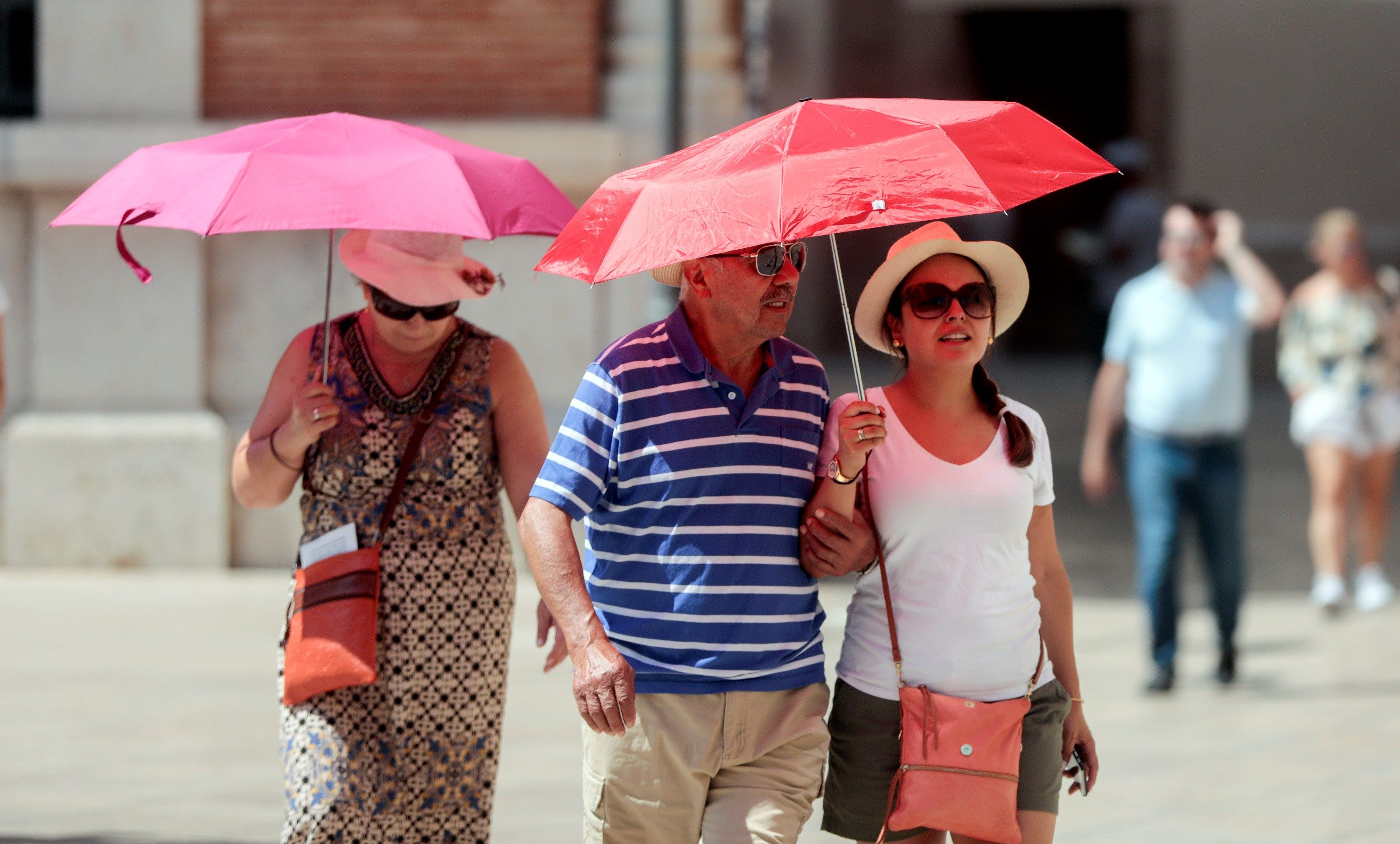Varias personas recorren el casco antiguo de Valencia protegidos con parasoles