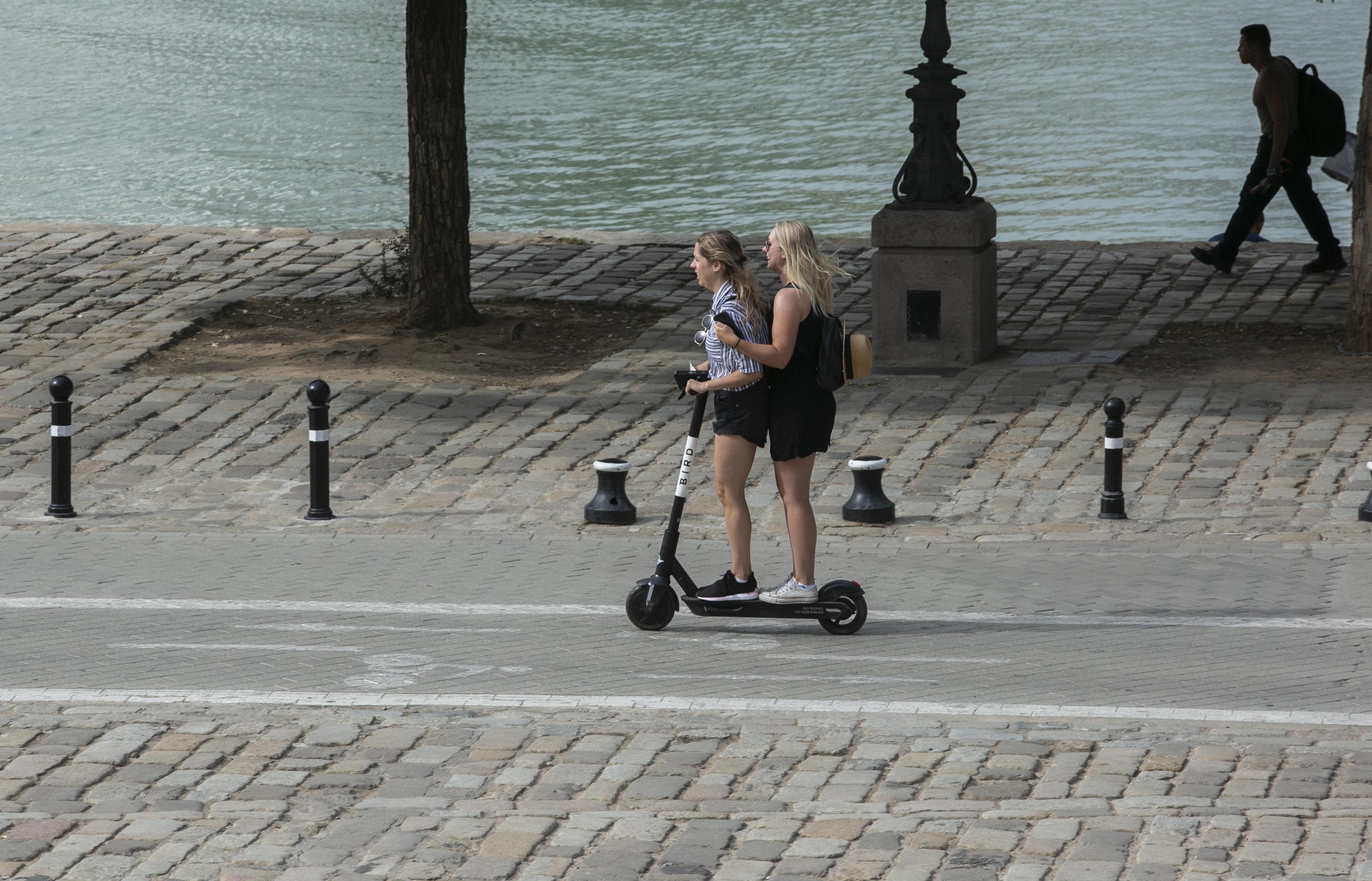 Una pareja de mujeres subidas en un sólo patinete eléctrico circulan por el carril. EP