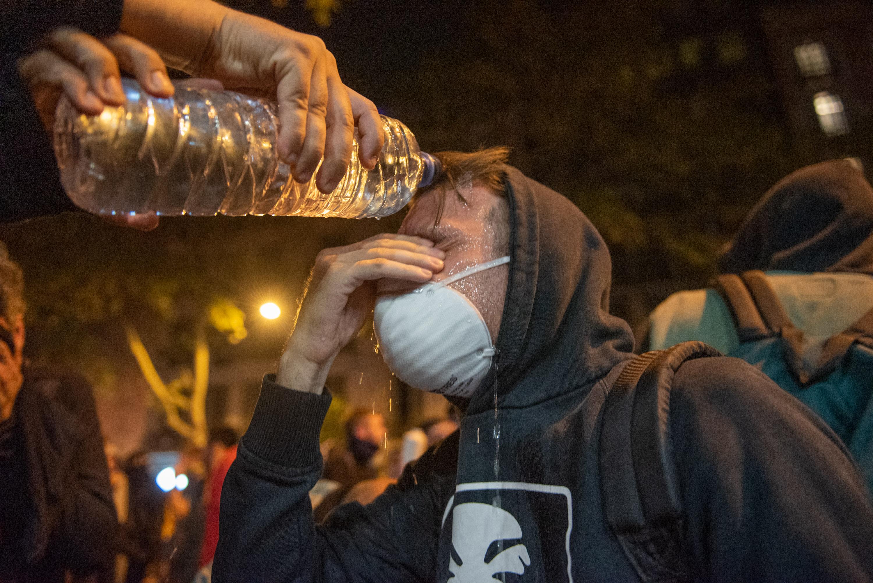 Un manifestante echa agua a otro con una mascarilla blanca durante los disturbios en la Plaza de Urquinaona en Barcelona a 18 de octubre de 2019 
