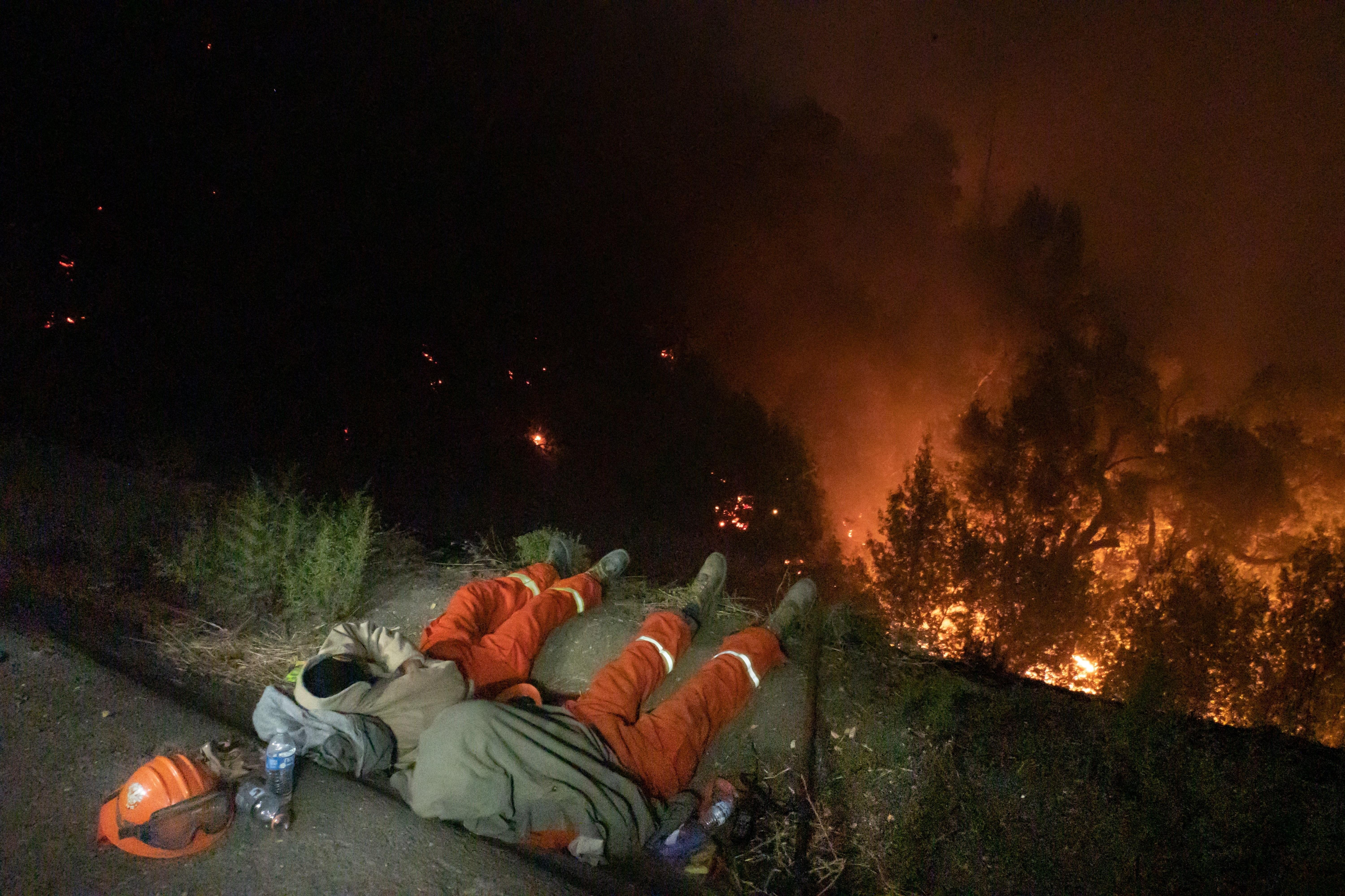 Dos bomberos descansan con el fuego a sus pies en California