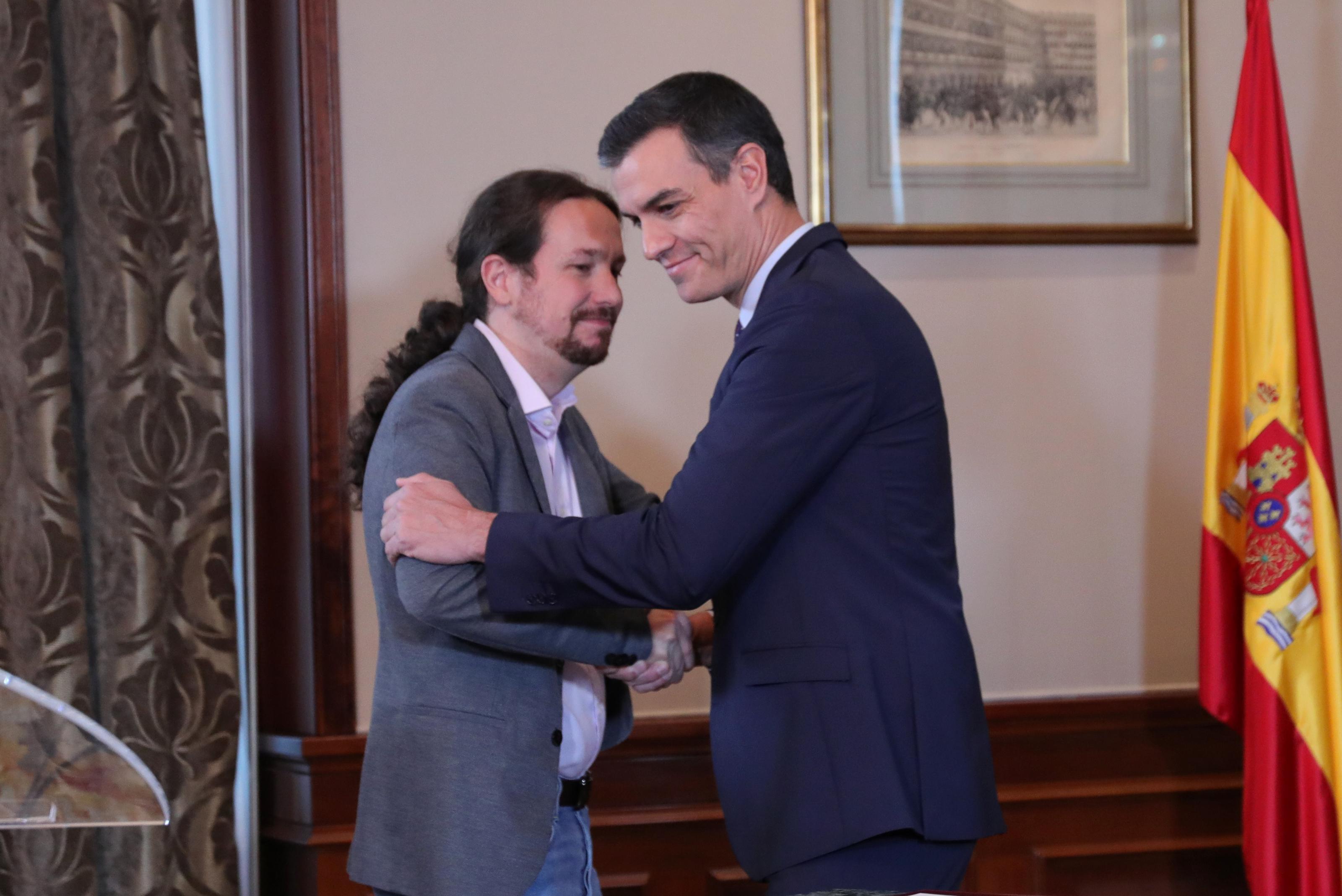 El presidente del Gobierno en funciones Pedro Sánchez y el líder de Podemos Pablo Iglesias se abrazan en el Congreso de los Diputados después de firmar el acuerdo de coalición.